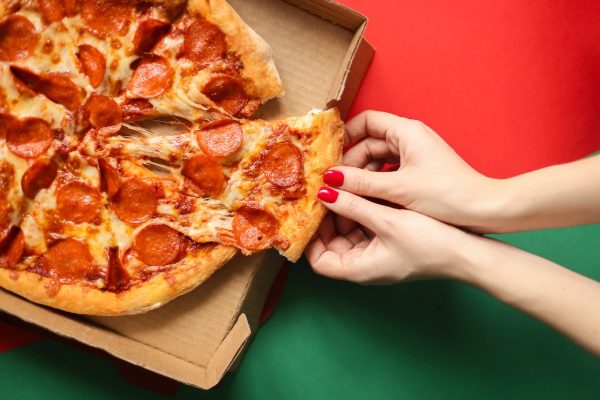 Hands grabbing slice of medium pepperoni pizza